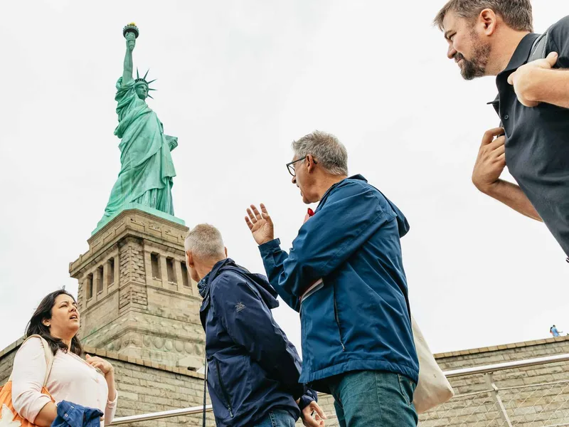 A guide explaining Ellis Island history to a small group near the Statue of Liberty in New York